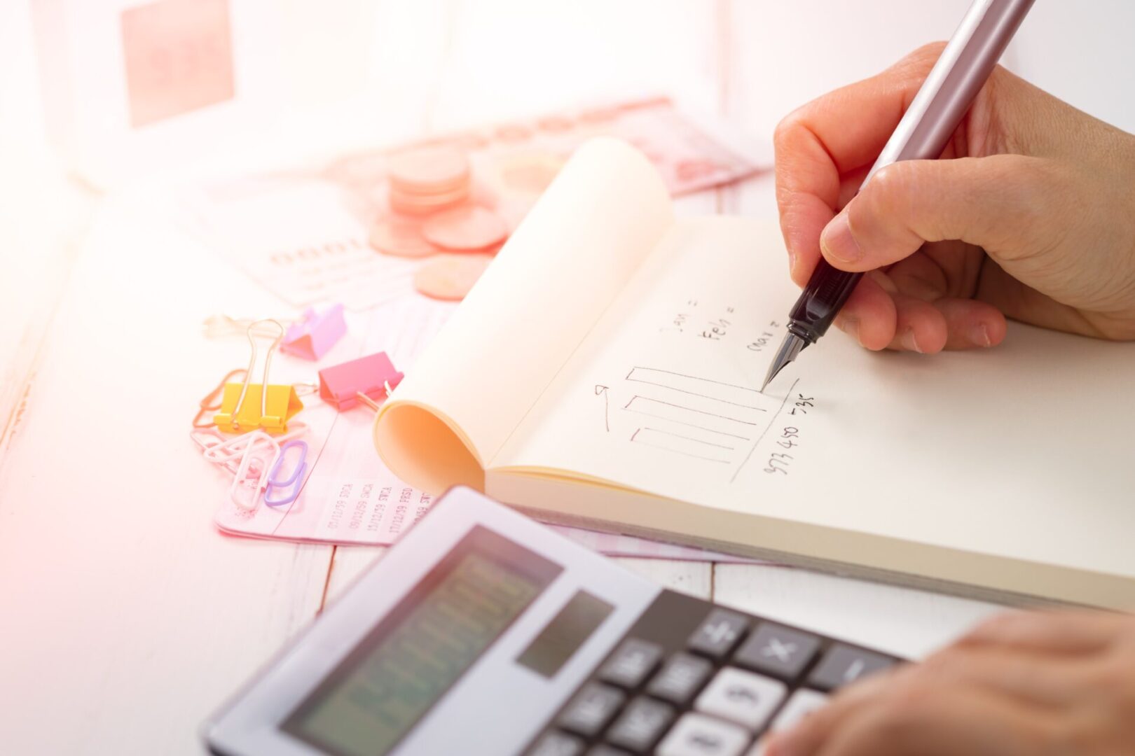 A person writing in a notebook next to an open calculator.